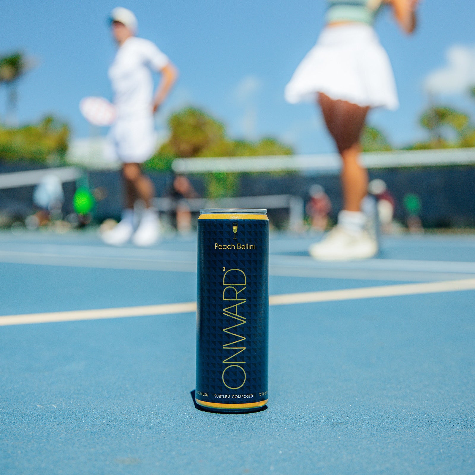 Onward Peach Bellini can on a tennis court with players in the background