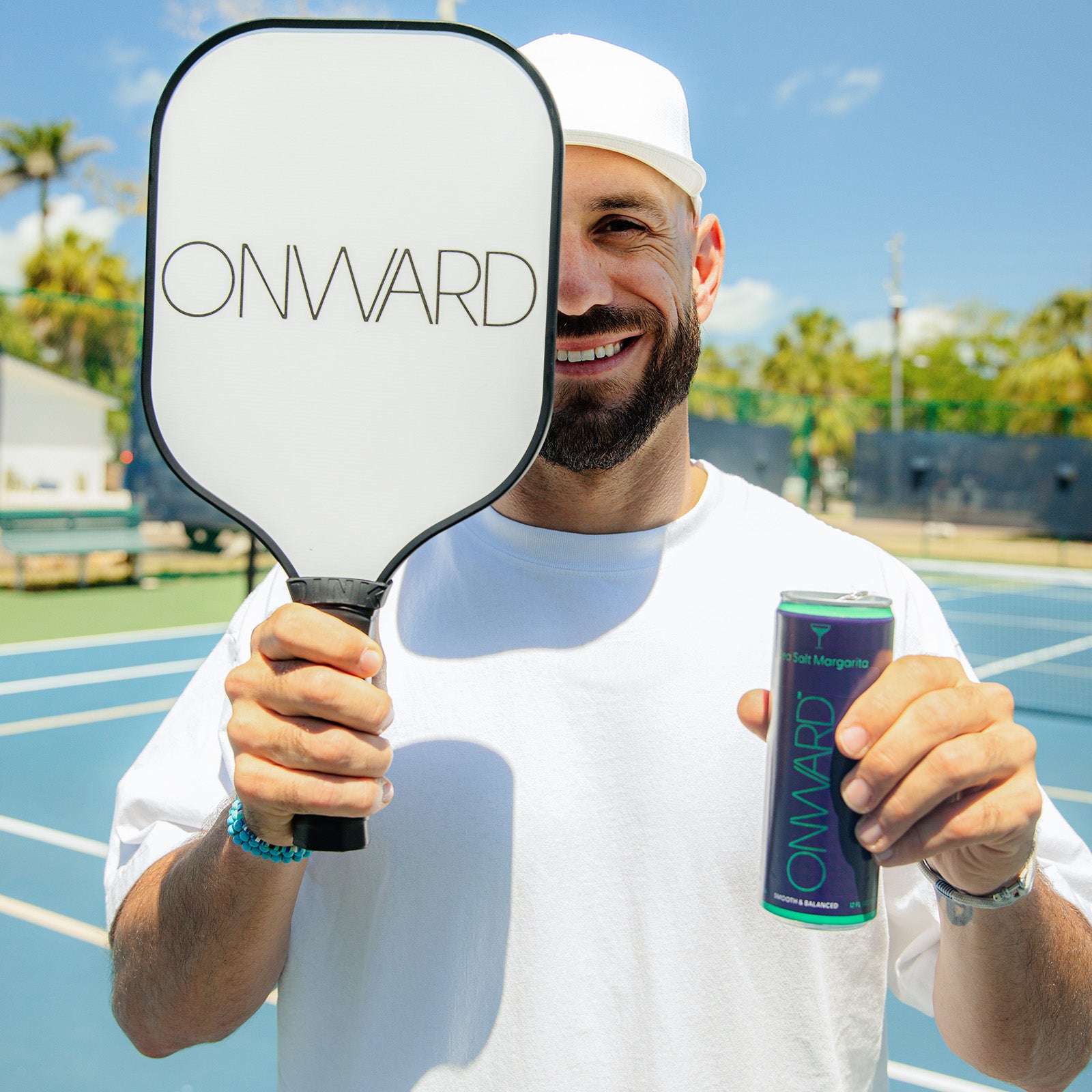 Man holding a paddle and a can with 'ONWARD' branding on a tennis court.