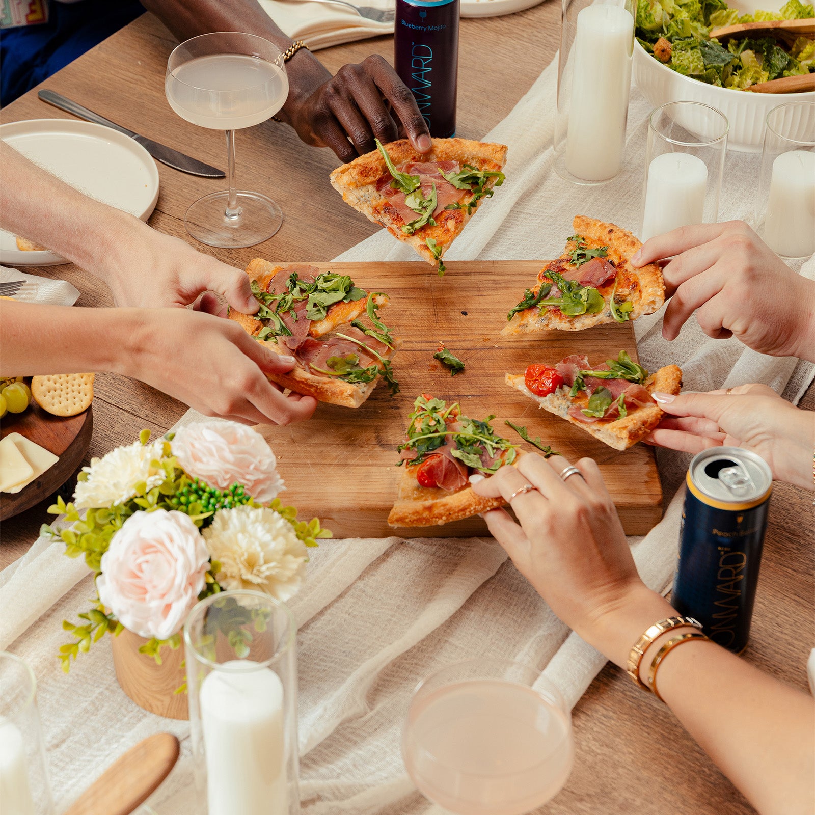 People enjoying pizza slices at a table with drinks and flowers.