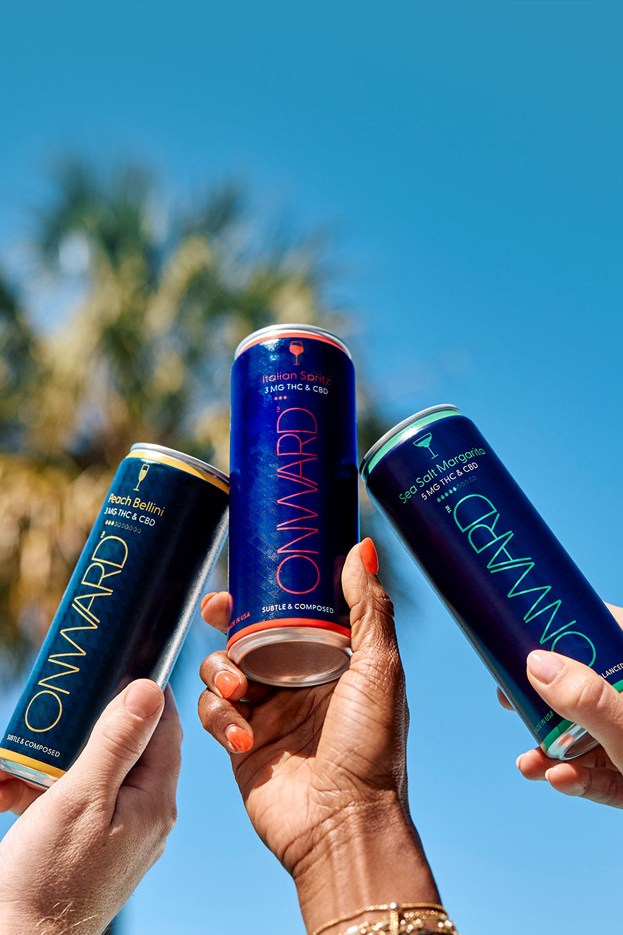 Three cans of 'Onward' energy drink held by people against a clear blue sky.