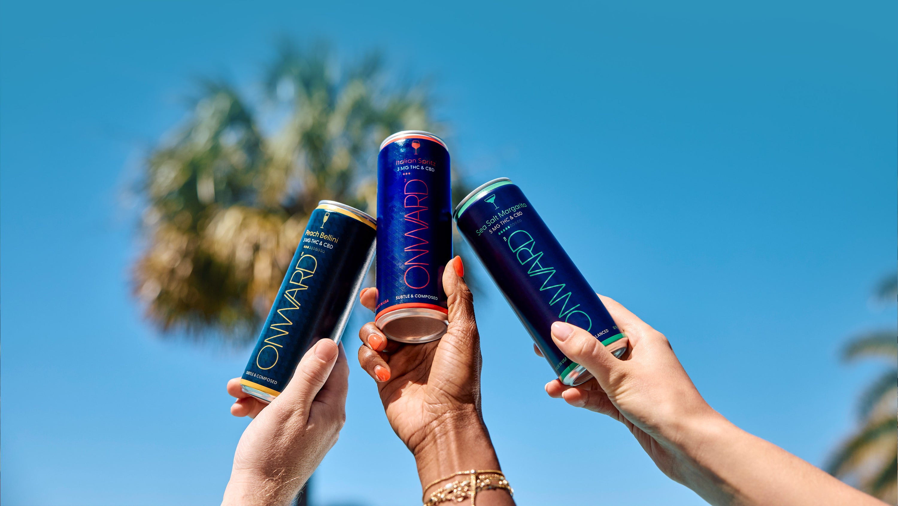 Three cans of 'Onward' against a clear blue sky with palm trees in the background